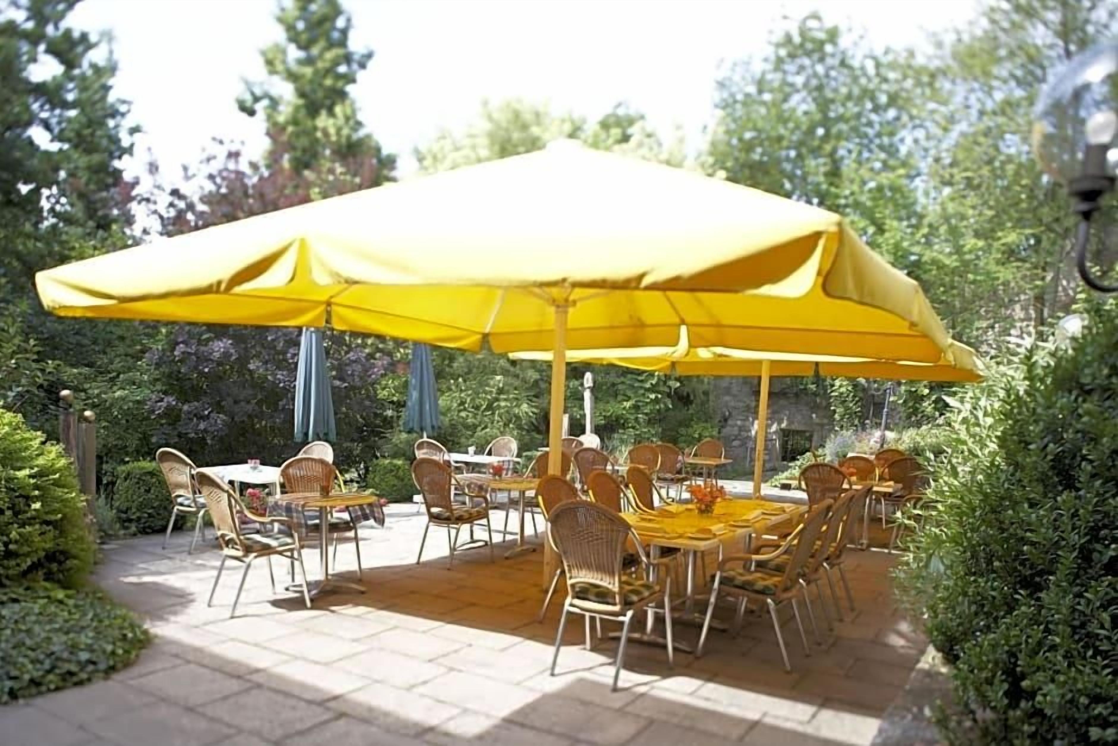 Un patio al aire libre con mesas y sillas bajo un amplio paraguas amarillo.