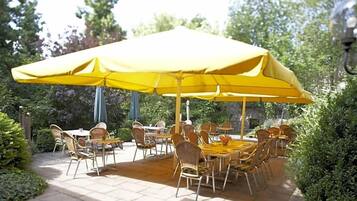 An outdoor patio with tables and chairs under a large yellow umbrella.