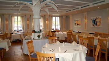 A dining area with round tables, chairs, and a high ceiling with decorative moldings.