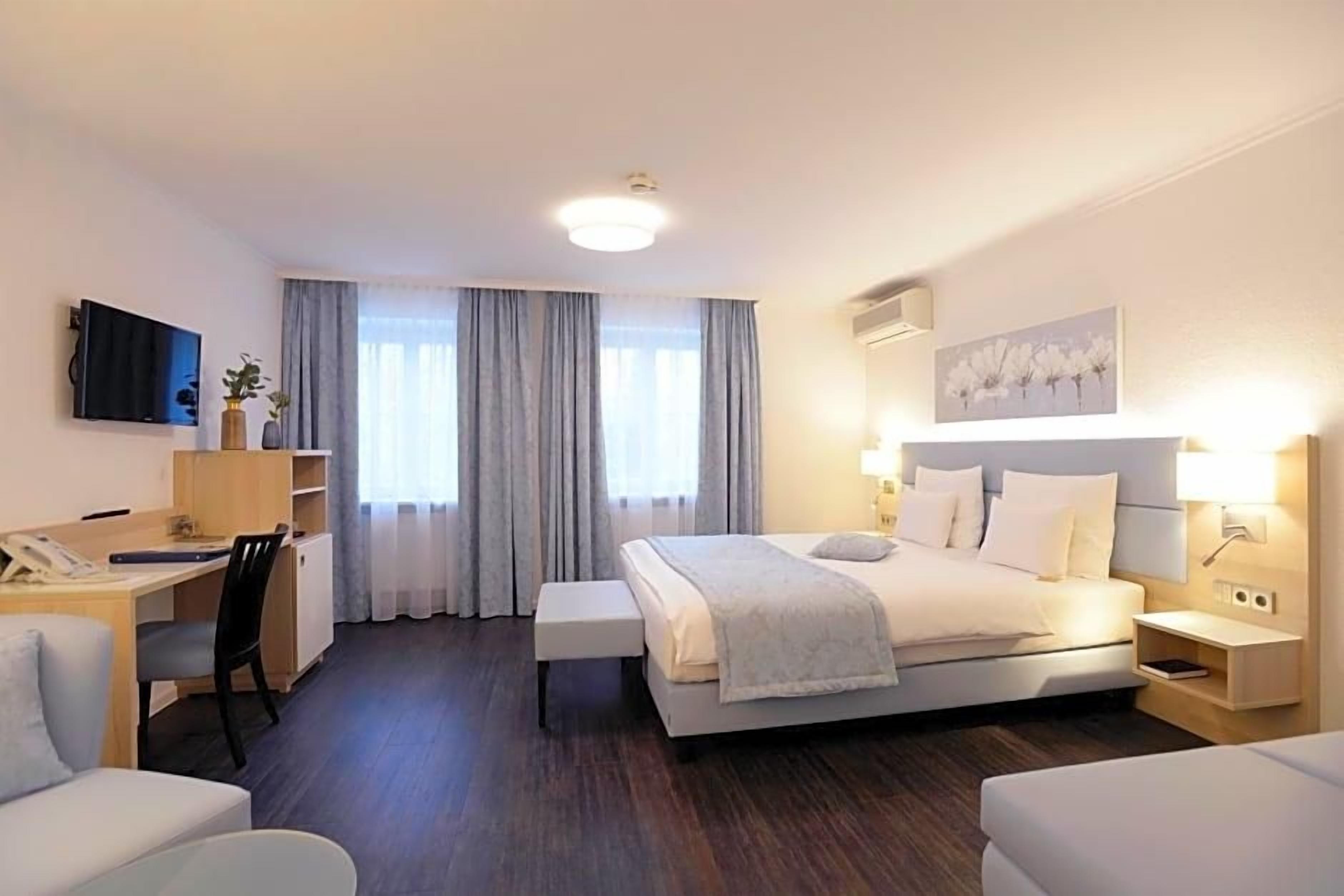 A hotel room with a bed, bedside table, desk, chair, and a TV.