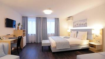 A hotel room with a bed, bedside table, desk, chair, and a TV.