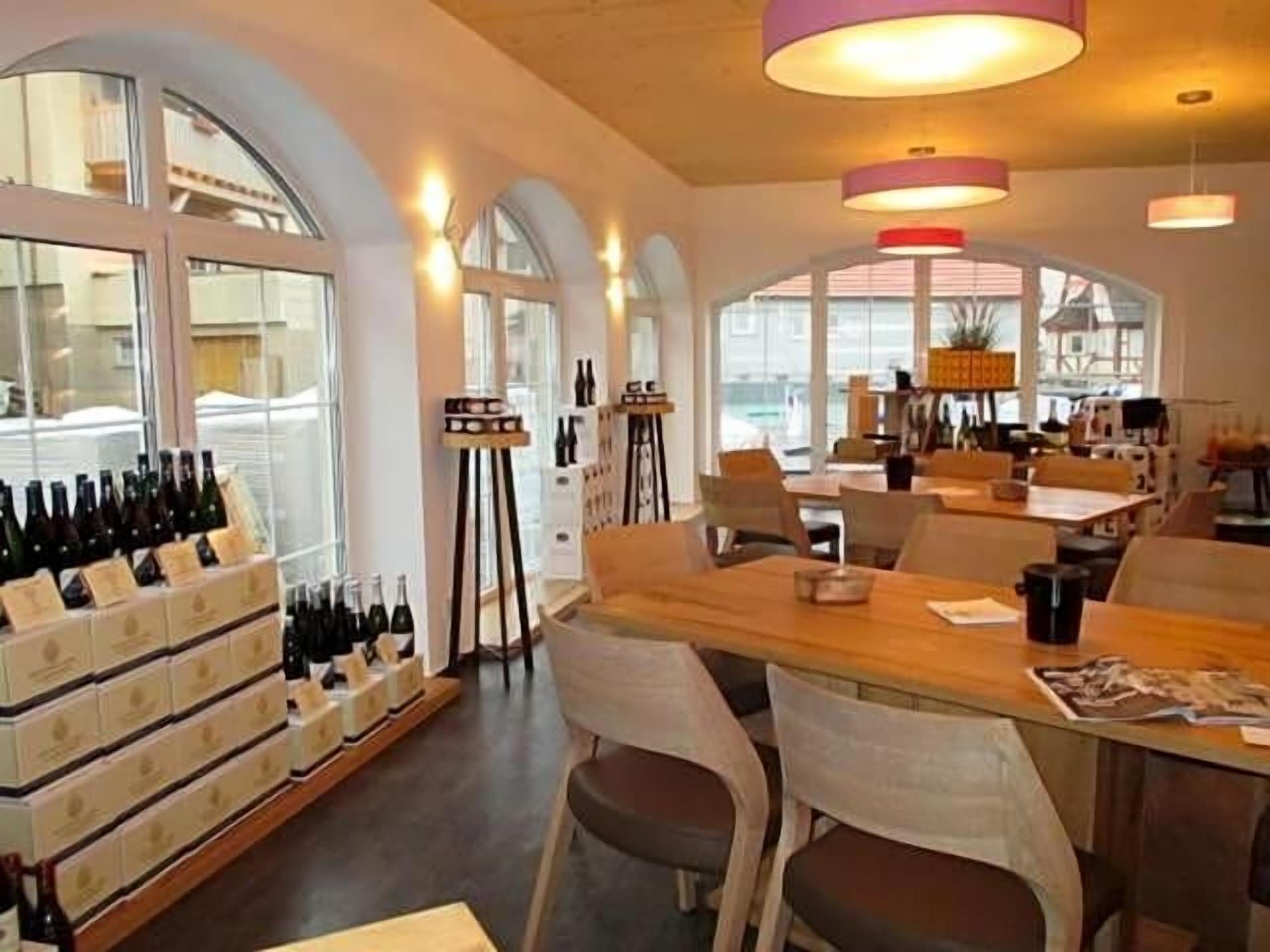 A restaurant with a long wooden table, chairs, and a wine display.