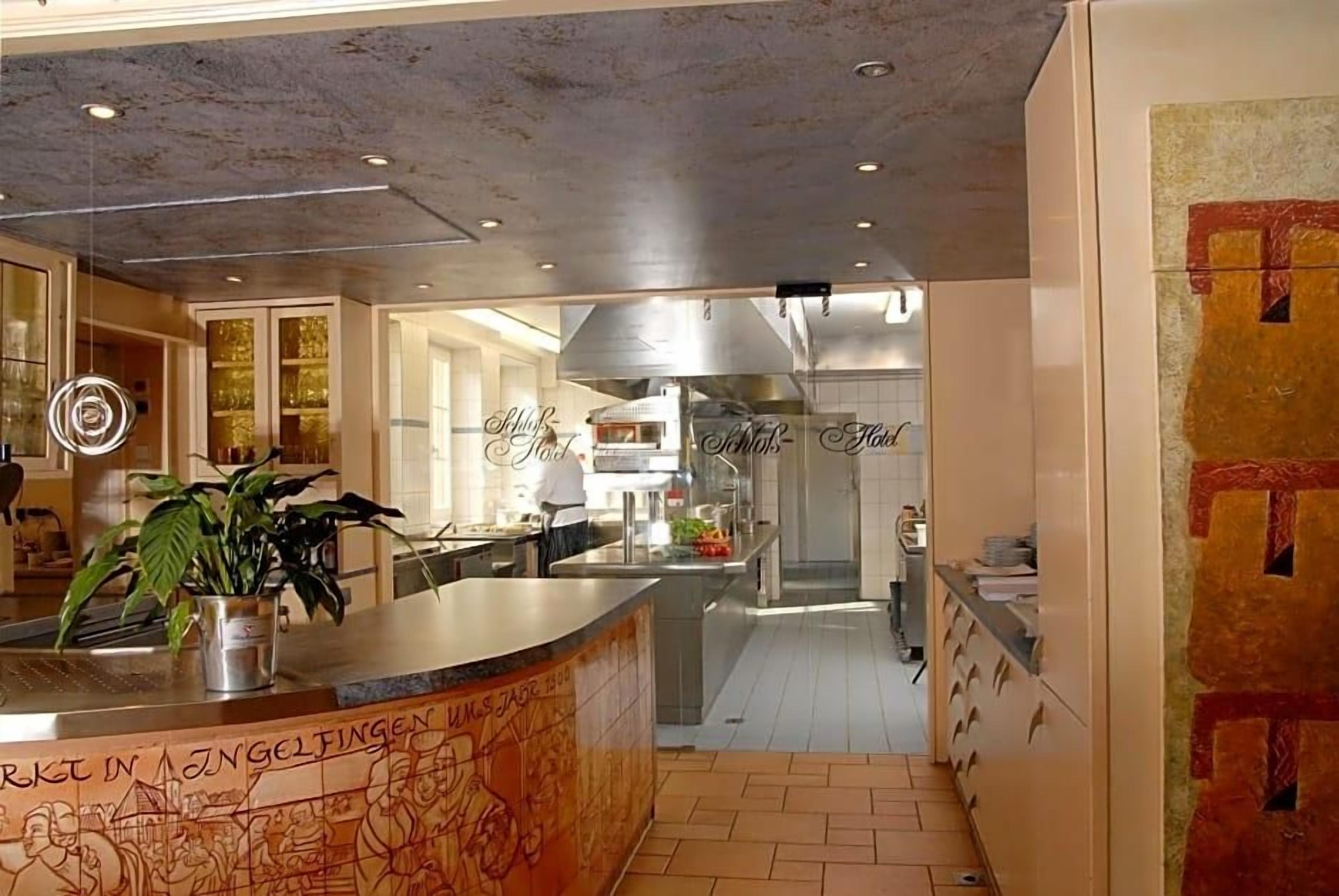 A hotel kitchen with stainless steel appliances, a bar area, and a counter with a plant.