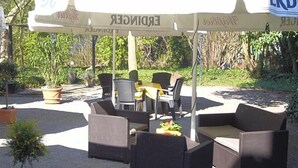 An outdoor seating area with wicker furniture under a canopy, surrounded by greenery. - Ackfeld Hotel Restaurant (Bueren)