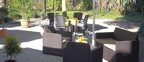 An outdoor seating area with wicker furniture under a canopy, surrounded by greenery.