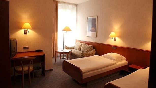 A hotel room with a bed, a desk, a chair, and two bedside lamps. - Ackfeld Hotel Restaurant (Bueren)