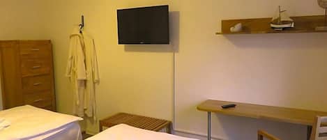 Quarto de hotel com duas camas, televisão fixada na parede, cômoda de madeira e uma pequena mesa com uma cadeira.