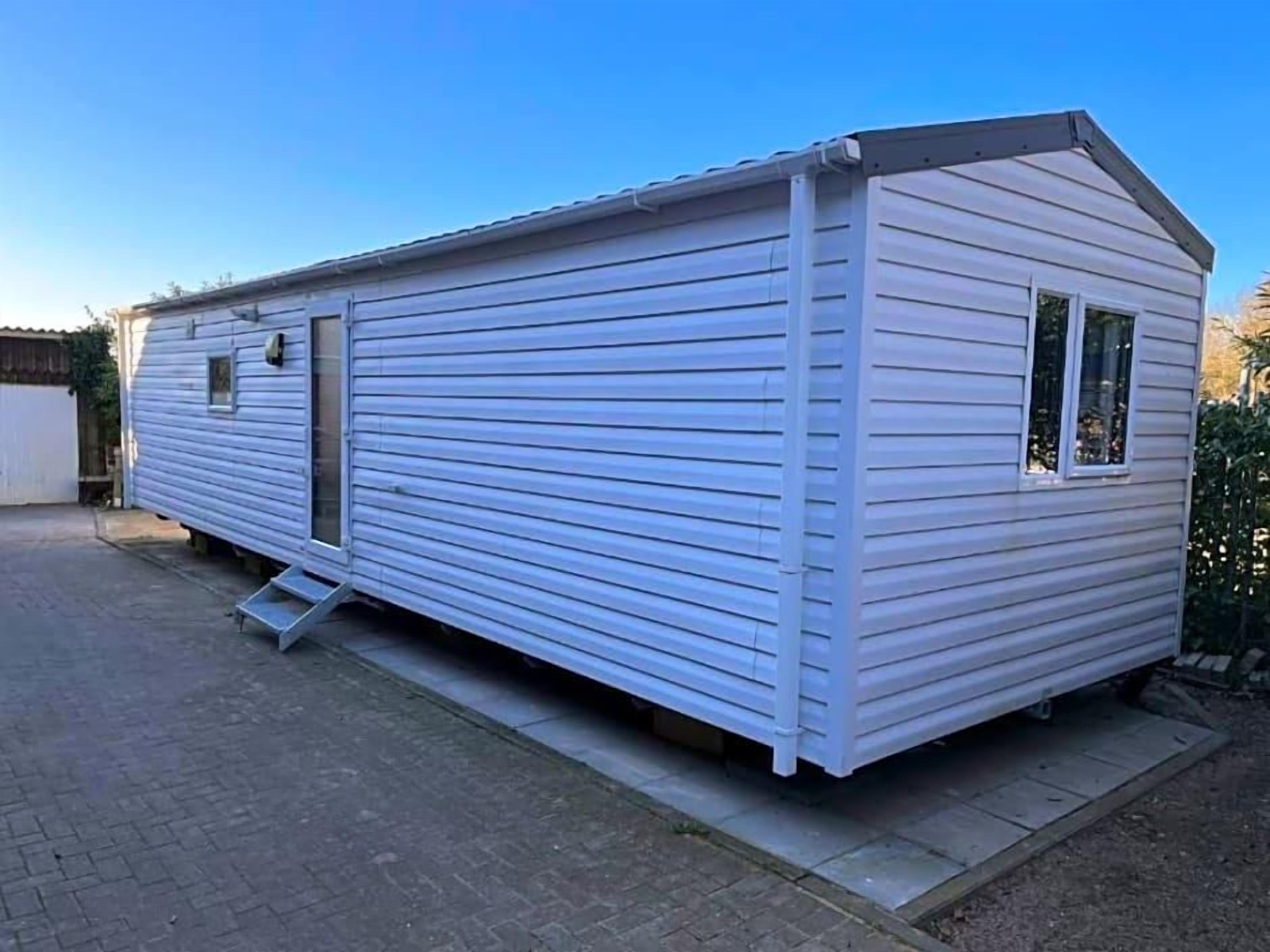 A single-story mobile home with a flat roof, a front door, and a small window.