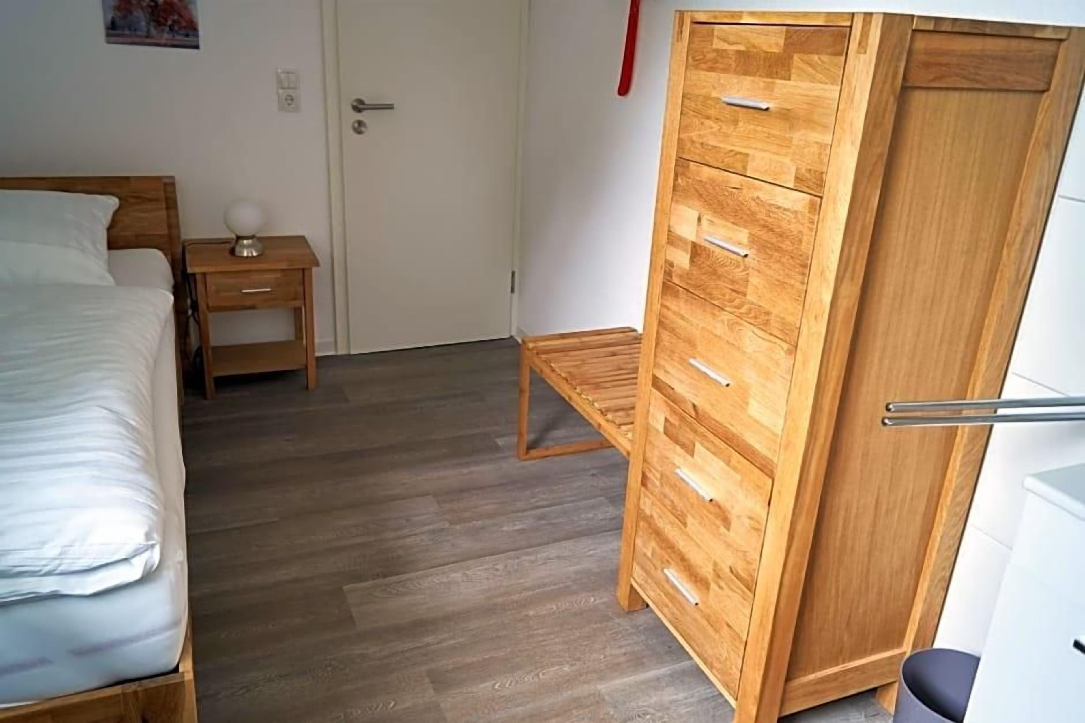 Un dormitorio con una cama, un armario de madera, una mesita de noche y un buró.