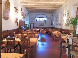 A restaurant with multiple tables and chairs, wooden beams on the ceiling, and various wall decorations.