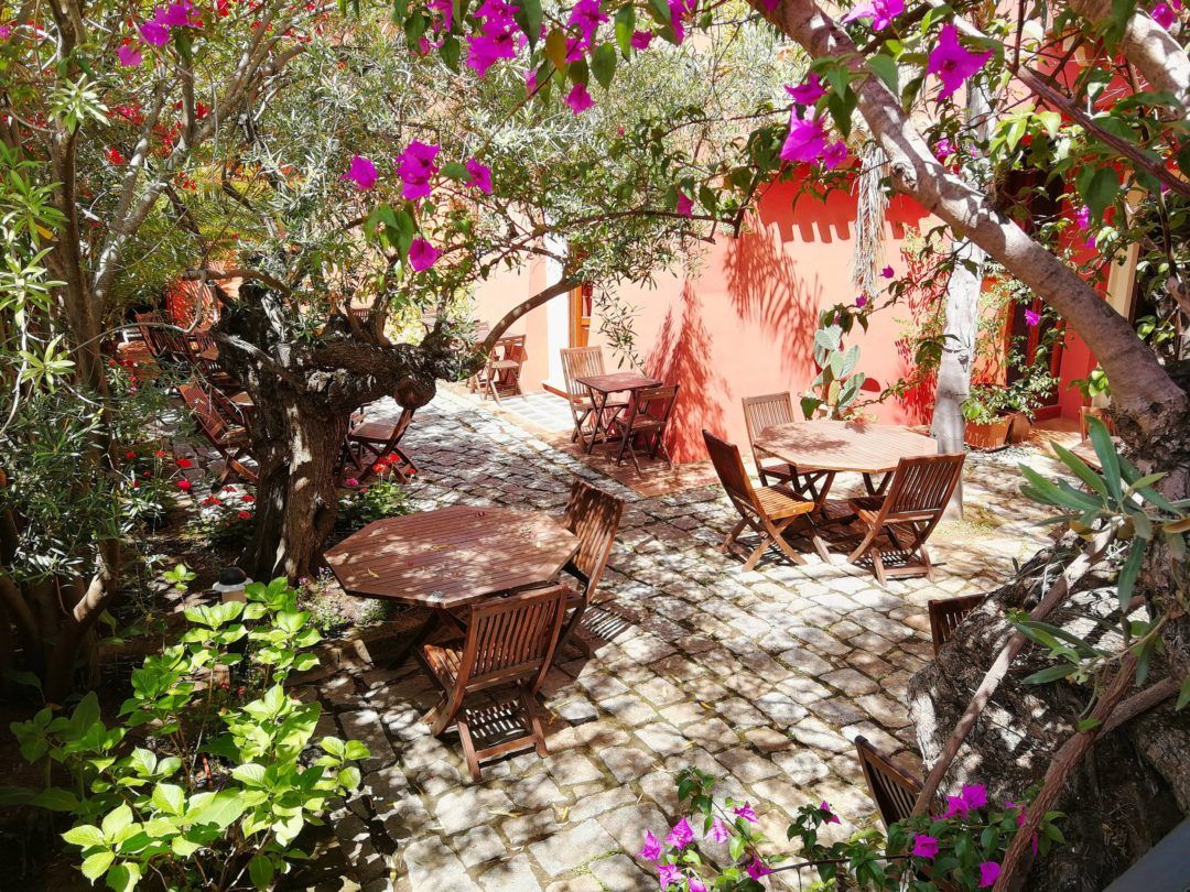 An outdoor patio with stone flooring, wooden furniture, and lush greenery.