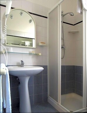 A bathroom with a pedestal sink, a mirror, a shower enclosure, and a towel rack.