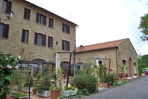 A stone building with multiple windows and a covered outdoor seating area with potted plants.