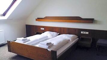 Een enkel bed met houten frame en hoofdbord, een nachtkastje en een kleine stoel in een kamer met een schuine plafond en dakraam.