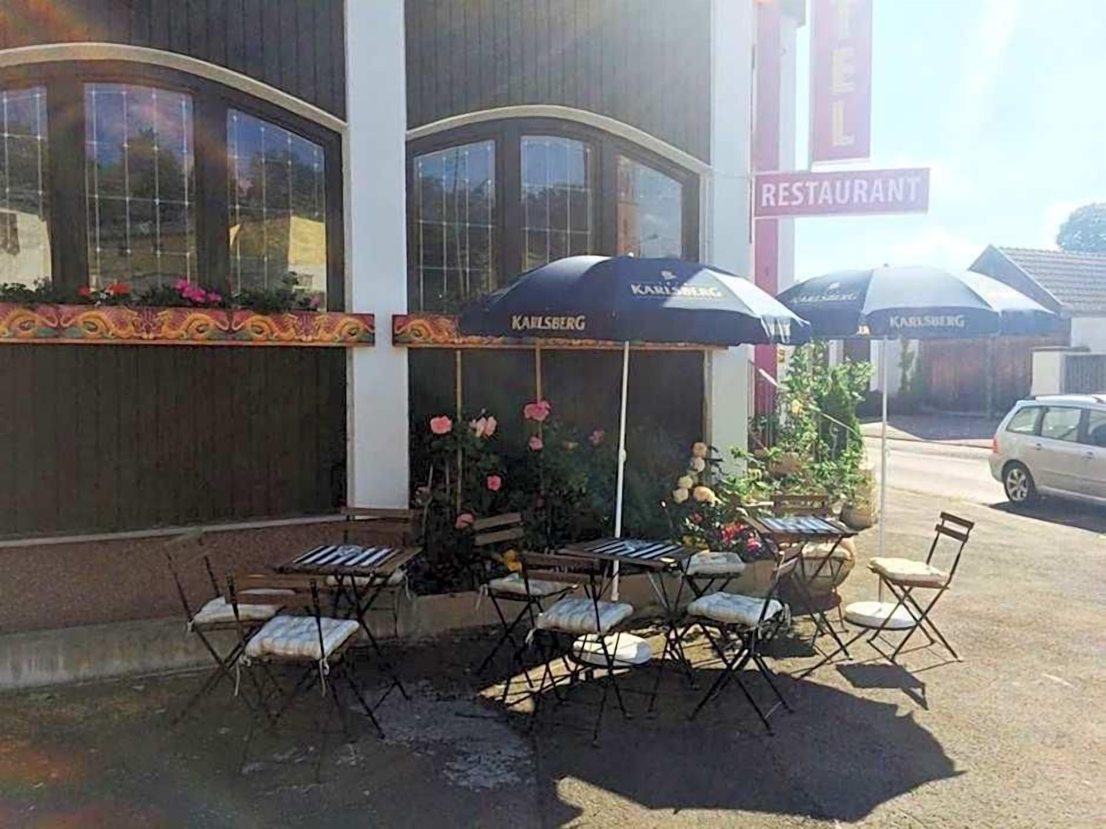 Een terras met tafels en stoelen, een bloembed en een gebouw met een 'RESTAURANT' bord.