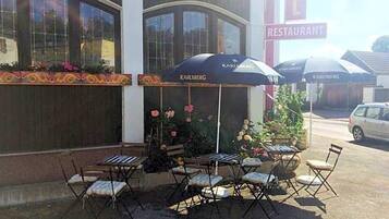 Een terras met tafels en stoelen, een bloembed en een gebouw met een 'RESTAURANT' bord.
