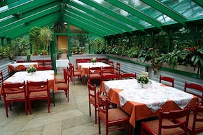 A greenhouse-style dining area with tables and chairs, surrounded by potted plants.