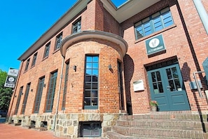 A brick building with a curved corner, a green door, and a sign for 'ALTEHEIMAT.' - Alte Heimat (Berge)