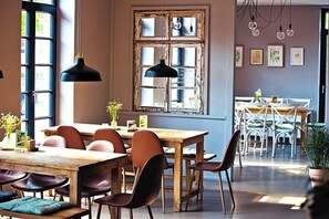 A dining area with a wooden table and chairs, a large window with a view, pendant lighting, and framed artwork on the wall. - Alte Heimat (Berge)