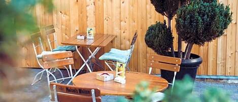 A wooden outdoor seating area with a table and chairs, a potted plant, and a wooden wall.