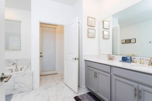 Un baño con tocador blanco, un espejo grande y una puerta que da a otra habitación.