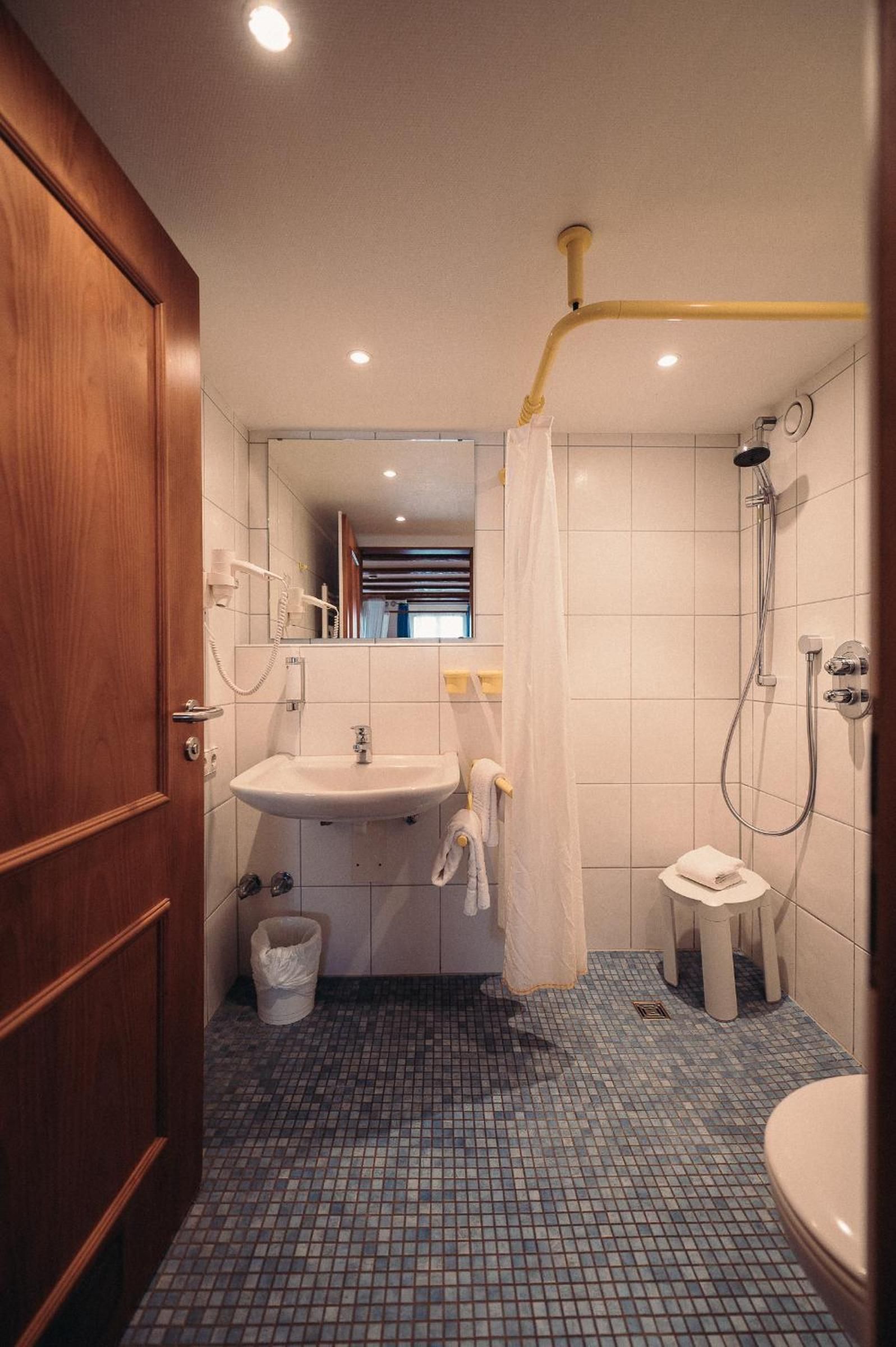 Ein Badezimmer mit Holztür, Waschbecken, Spiegel, Dusche und Toilette.