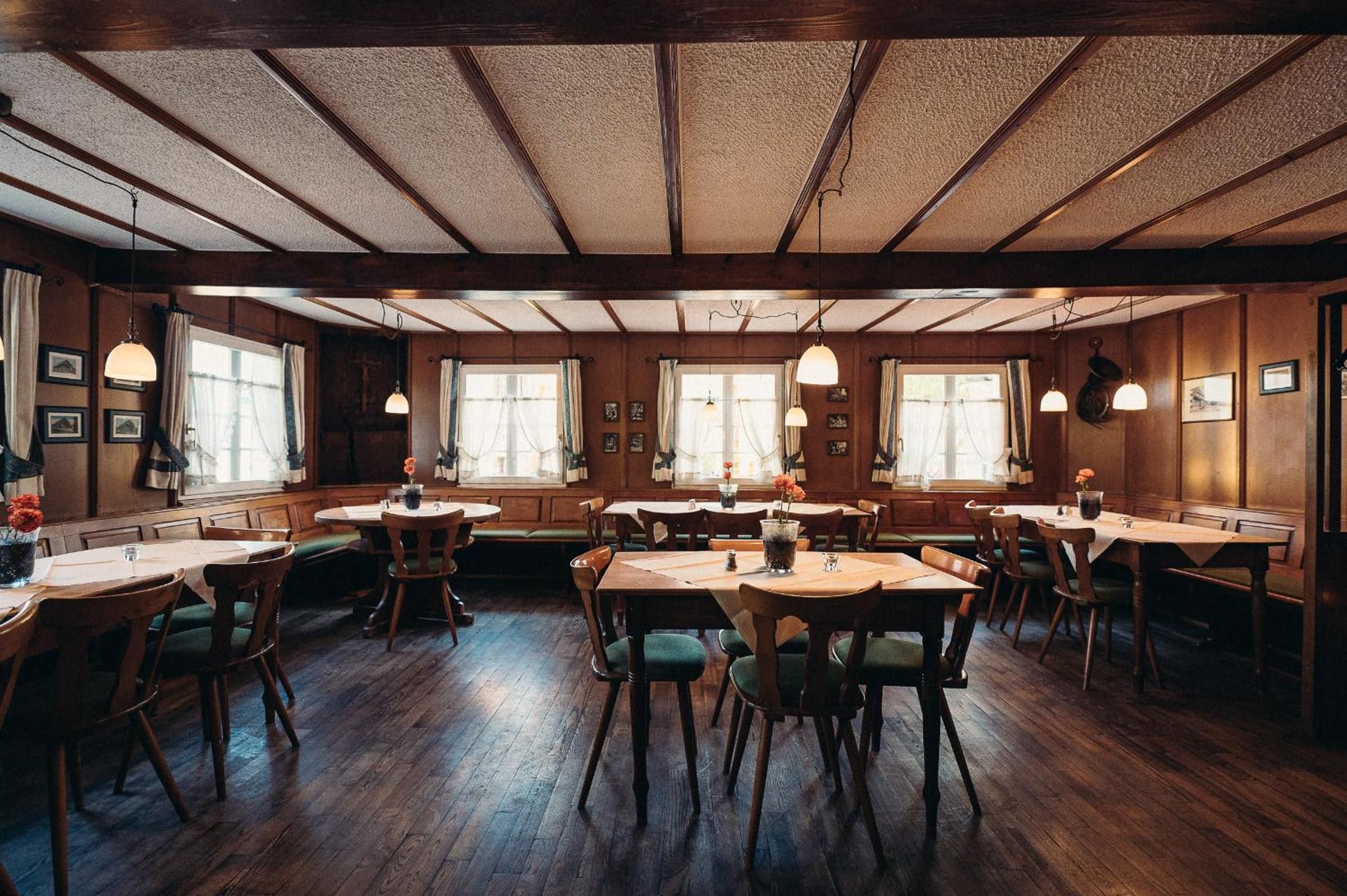Ein Restaurant mit Holztischen und -stühlen, großen Fenstern und hängenden Pendelleuchten.
