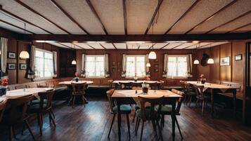 Ein Restaurant mit Holztischen und -stühlen, großen Fenstern und hängenden Pendelleuchten.