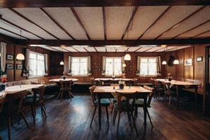 A restaurant with wooden tables and chairs, large windows, and hanging pendant lights. - Hofgut Himmelreich (Kirchzarten)