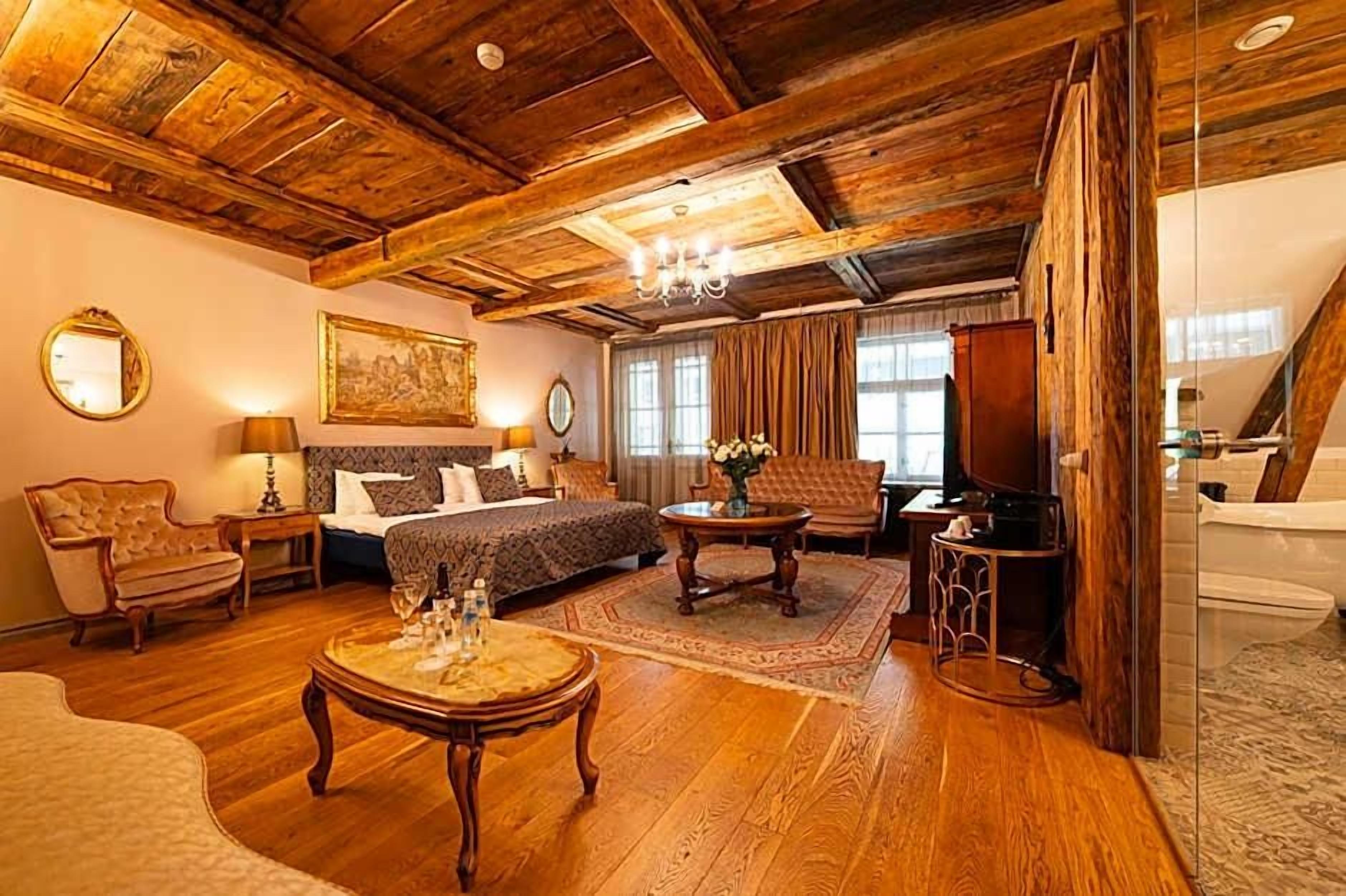 Una habitación con techo de madera, cama con ropa de cama estampada, una zona de estar con una mesa y sillas, y un ventanal grande.