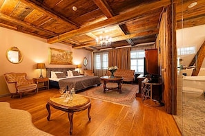 A room with a wooden ceiling, a bed with patterned bedding, a sitting area with a table and chairs, and a large window. - Boutique Hotel Virkas Mui A (Kuldīga)