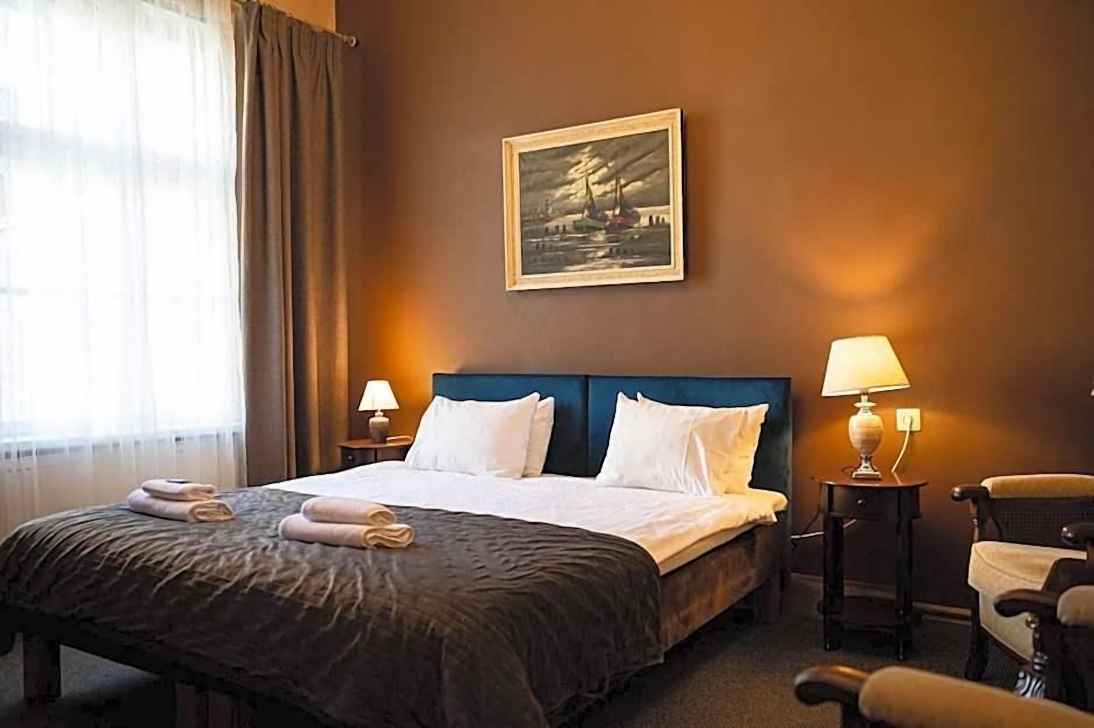 Quarto de hotel com uma cama, duas mesas de cabeceira, uma cadeira e um quadro na parede.