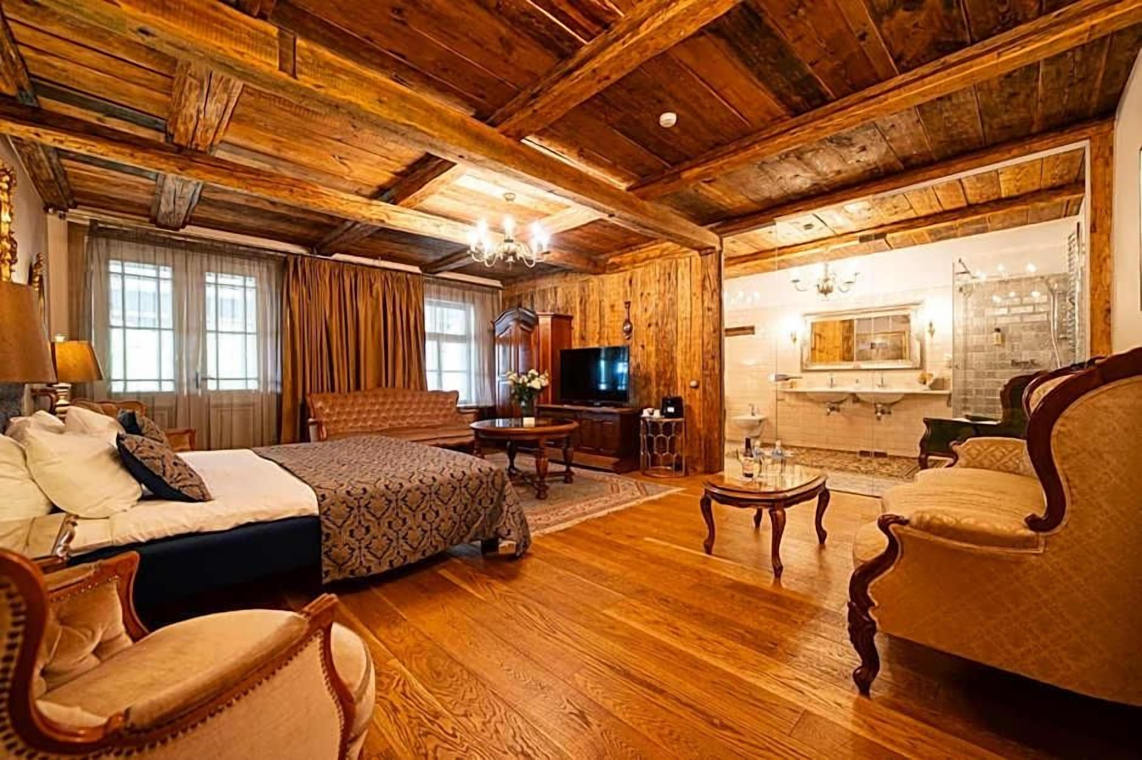 Una habitación con suelo de madera, con cama, sofá, televisor y zona de comedor.