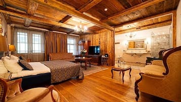 Una habitación con suelo de madera, con cama, sofá, televisor y zona de comedor.