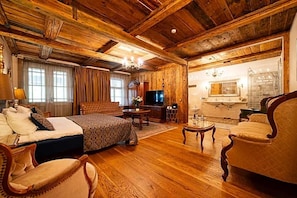 A wooden-floored room with a bed, a sofa, a television, and a dining area.
