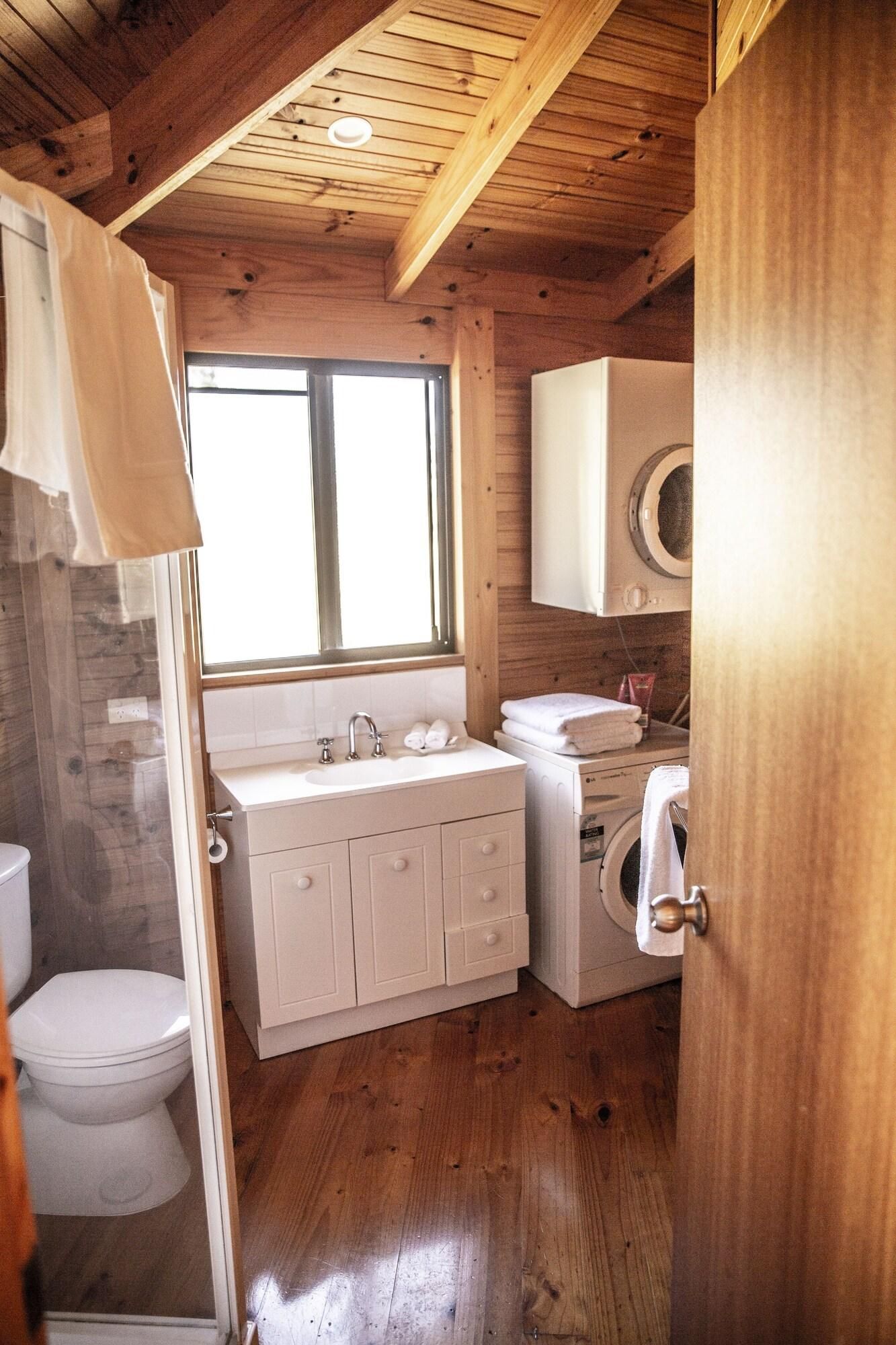 A compact bathroom with a wooden ceiling, a toilet, a sink with cabinets, and a washing machine.