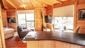 A wooden cabin interior with a dining area, a sofa, a TV, and a view of the outdoors.