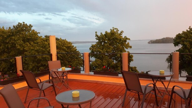 An outdoor deck with tables and chairs, overlooking a body of water and trees. - Seehotel Bad Kleinen (Bad Kleinen)