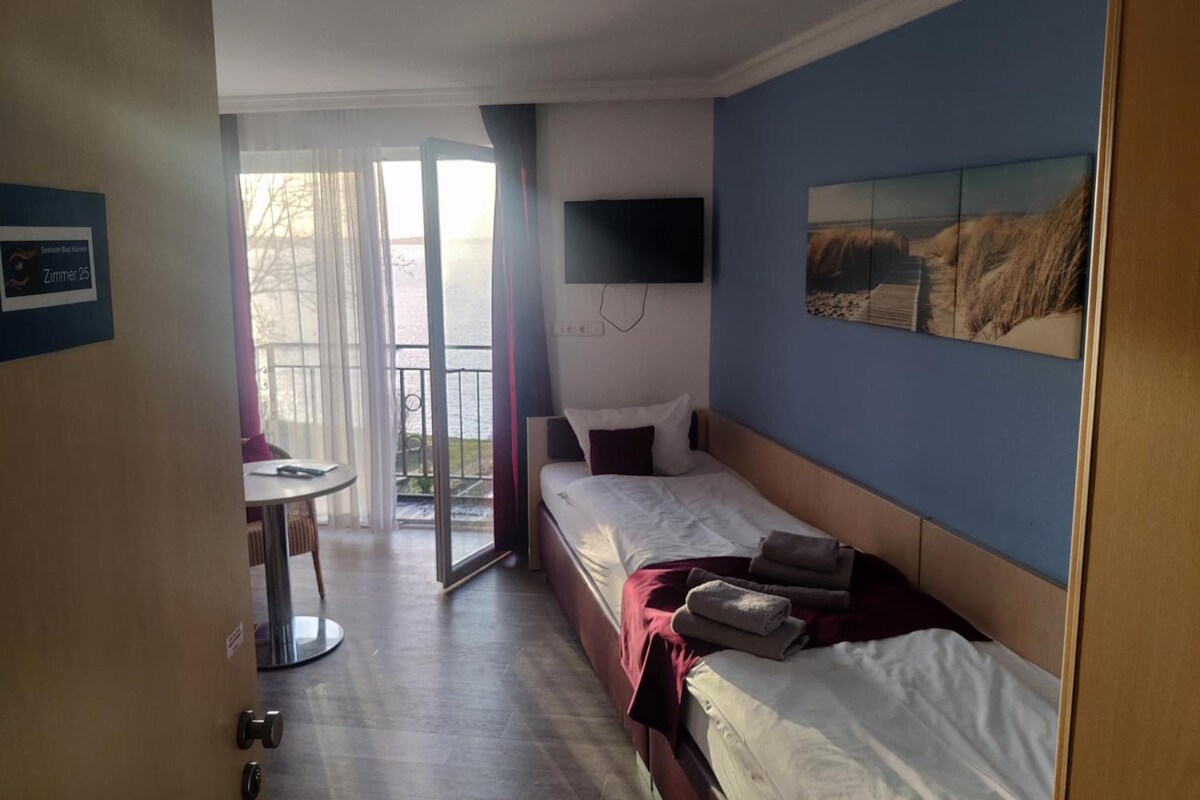 A hotel room with a bed, a TV mounted on the wall, a small table, and a view of the outdoors through a glass door.
