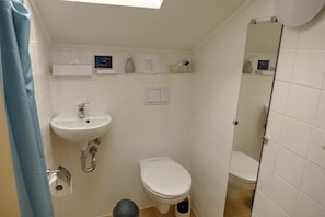 A small bathroom with a white sink, toilet, and shower. There are toiletries on the wall and a mirror. - Seehotel Bad Kleinen (Bad Kleinen)