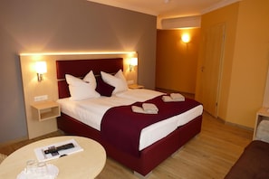 A hotel room with a large bed, two bedside tables, a round table with a remote control, and a door. - Seehotel Bad Kleinen (Bad Kleinen)