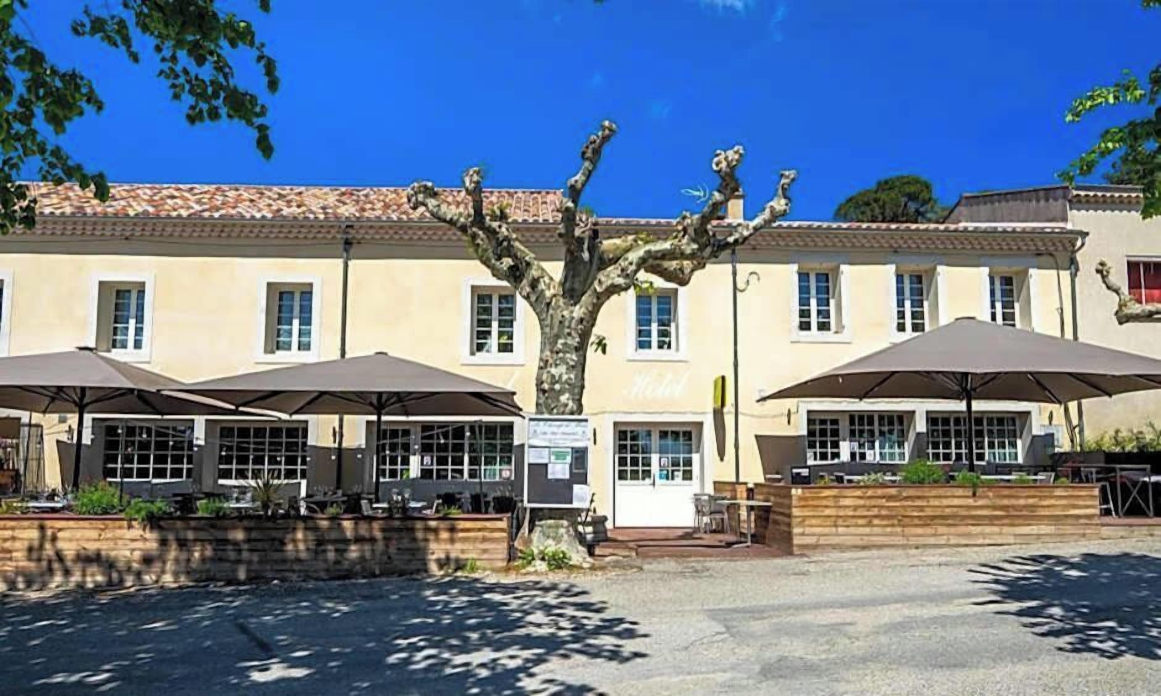 A building with a tiled roof, outdoor seating with umbrellas, and a tree in front.