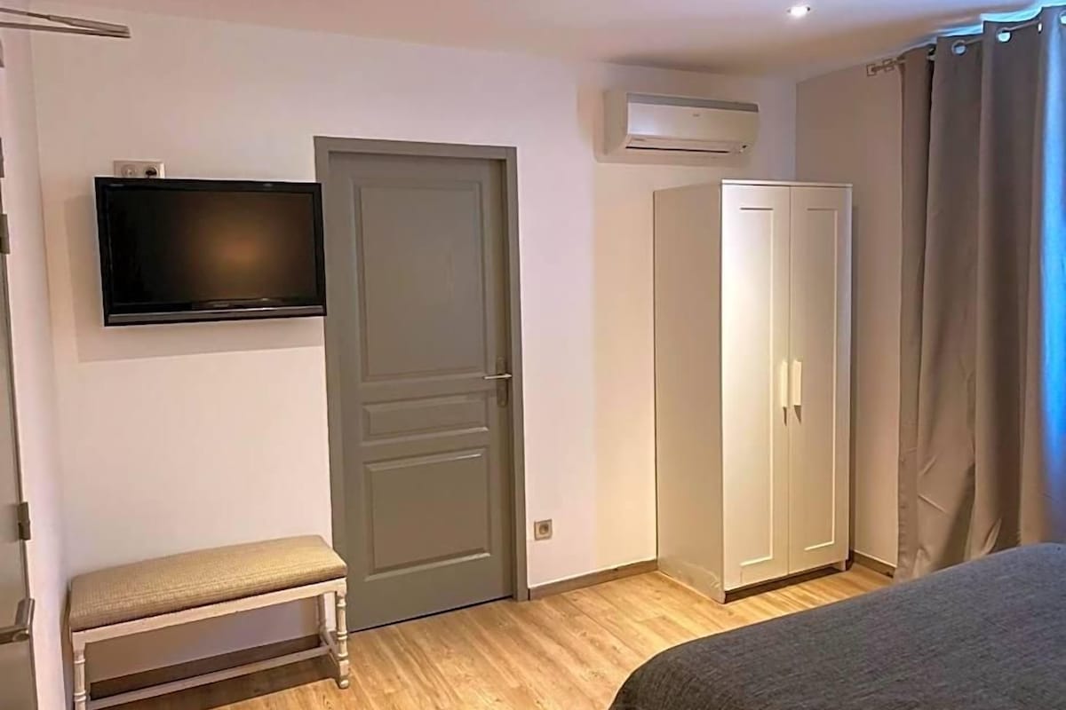 A bedroom with a bed, a bench, a wardrobe, a television, and an air conditioning unit.