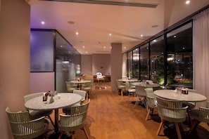 Un espace de restauration moderne avec des tables et des chaises rondes, de grandes fenêtres offrant une vue dégagée et un plancher en bois.