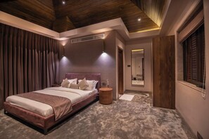 Ein Schlafzimmer mit einem großen Bett, einem runden Holfnischchen, einem Spiegel und einem Fenster mit Jalousien.