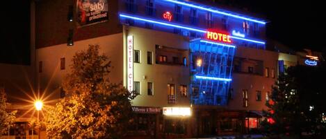 Um hotel com um letreiro grande escrito 'HOTEL', uma entrada visível e uma árvore em primeiro plano.