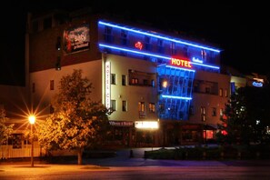 Um hotel com um letreiro grande escrito 'HOTEL', uma entrada visível e uma árvore em primeiro plano.