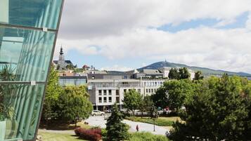 A modern building with a glass facade, a courtyard with trees, and a distant view of a church spire.