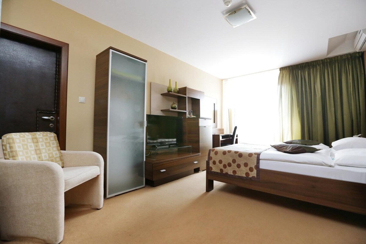 Quarto de hotel com cama, televisão, guarda-roupa, secretária e cadeira.
