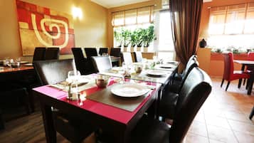A restaurant with a long table set for dining, chairs, and a large abstract painting on the wall.